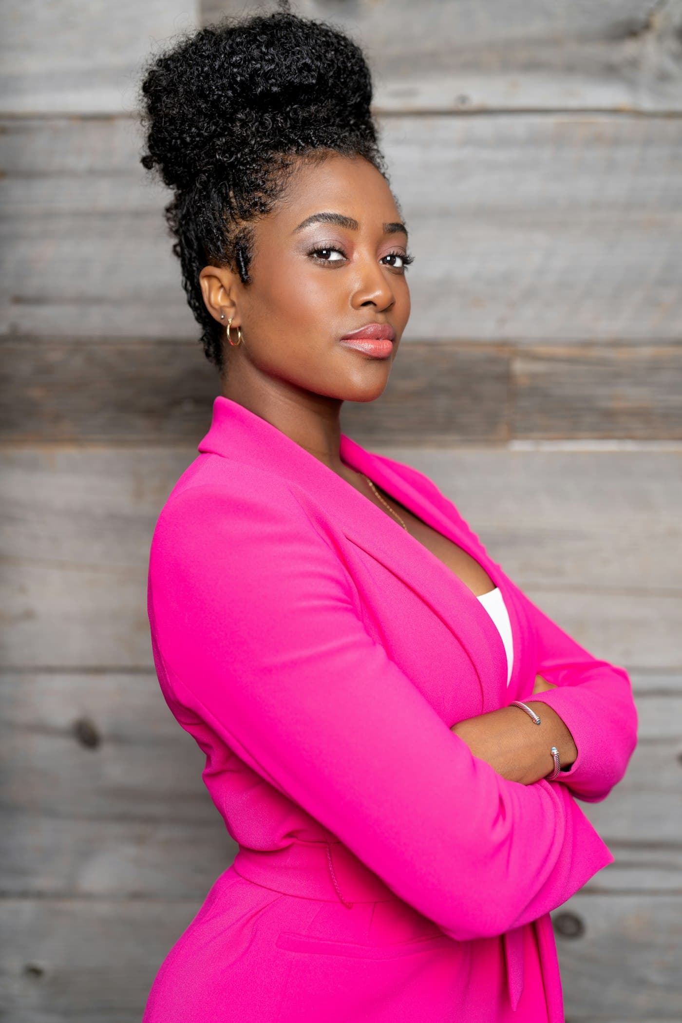 A confident woman in a bright pink suit, arms crossed, smiling softly