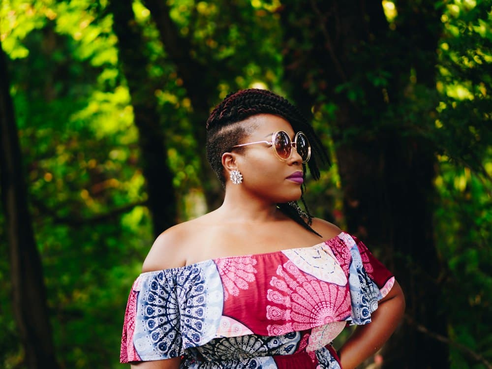 A woman in a pink patterned dress and sunglasses among green trees