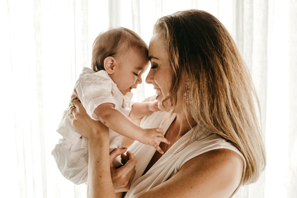 A smiling mother holding her baby close in soft window light