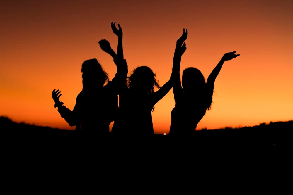 Silhouettes of three women dancing with raised arms at sunset